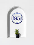 A decorative ceramic wall Address plaque featuring the house number '1851' in blue within a blue ornamental border, mounted on a white arched niche wall