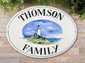 ceramic family name sign hand painted with a lighthouse on an island , blue ocean and sky  and two seagull flying
