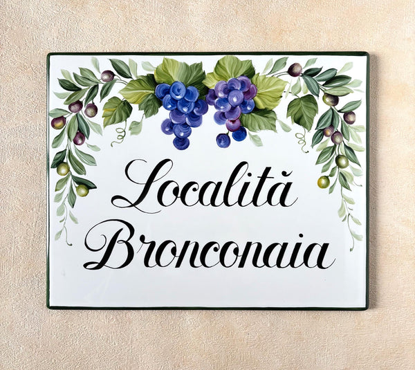 Rectangular Ceramic house name tile hand-painted with grapes, leaves and olives mounted on a beige wall