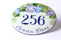 Oval-shaped address sign hand-painted with hydrangea design on a white background