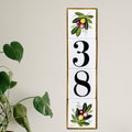 A vertical house numbers tile displaying '38' in black serif numerals, hand painted with olive branch at the top and bottom
