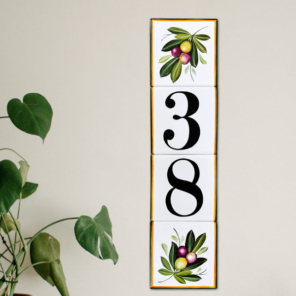 A vertical house numbers tile displaying '38' in black serif numerals, hand painted with olive branch at the top and bottom