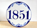 A round white ceramic house number sign with blue decorative border and the number 1851 in blue