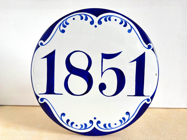 A round white ceramic house number sign with blue decorative border and the number 1851 in blue
