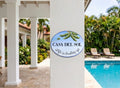 An oval decorative wall sign reading 'CASA DEL SOL' and 'Life is looking up' with green palm leaves, mounted on a white pillar in a resort-like setting with a swimming pool and palm trees in the background.