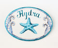 ceramic oval beach house sign, hand painted with a blue and tea starfish in center, two mosaic waves on each side and the name is painted on top in blue color 