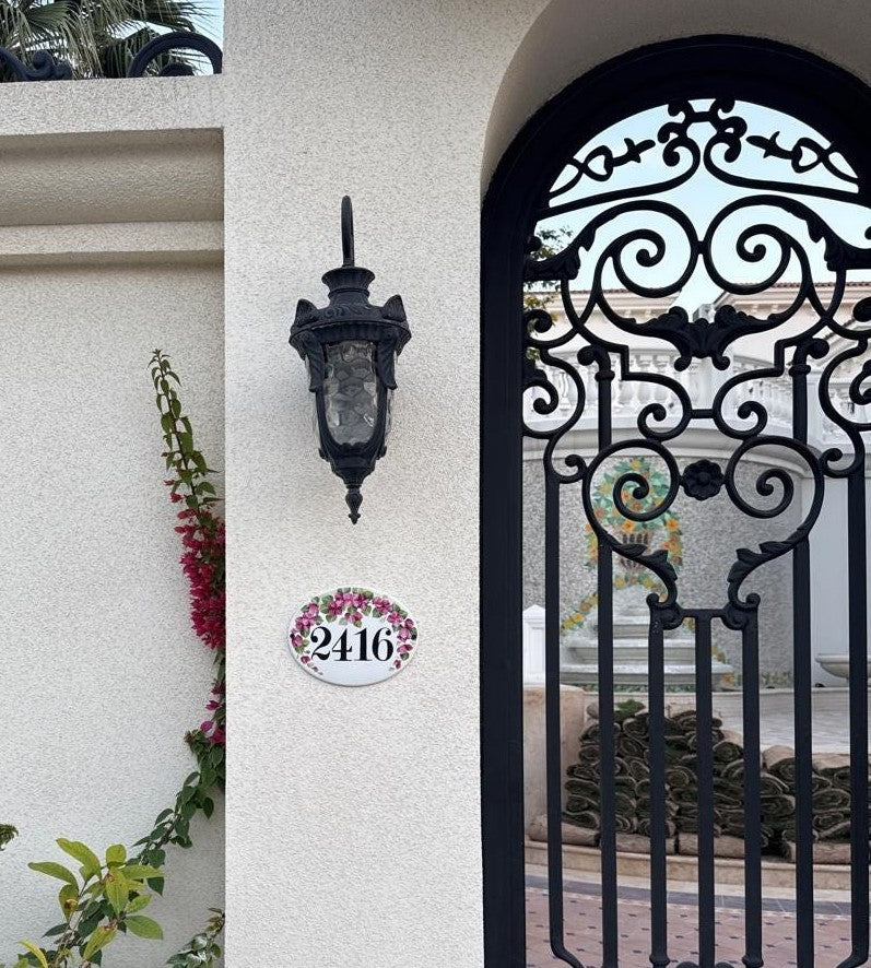 ceramic house number plaque hand painted with pink bougainvillea flowers mounted on a white wall