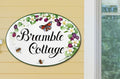 ceramic oval house sign hand-painted with blackberries, white flowers, bees and a red butterfly, mounted on a front door