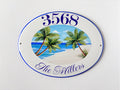 ceramic address plaque oval shaped hand painted with an ocean view, a beach and palm trees. the house number is painted curved on top in blue color