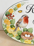A close-up of a decorative oval wall plaque or sign featuring a painted bird, nest with two white eggs, yellow flowers, green leaves, and a butterfly on a white background with black script lettering.