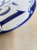 A close-up of a ceramic round address plaque with bold blue decoration painted around the border