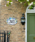 ceramic house number plaque hand-painted with blue hummingbird mounted on a brick wall