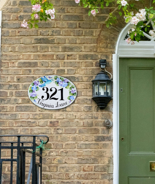 ceramic house number plaque hand-painted with blue hummingbird mounted on a brick wall