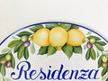 detail of a ceramic house sign hand painted with olives, yellow lemons and a blue border