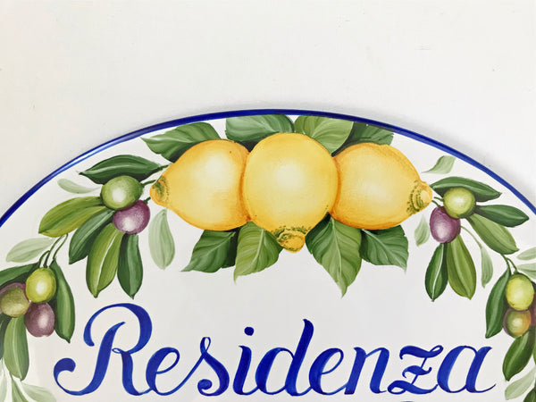 detail of a ceramic house sign hand painted with olives, yellow lemons and a blue border