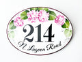 Oval-shaped house number plaque hand-painted with pink hydrangea and green leaves on a white background