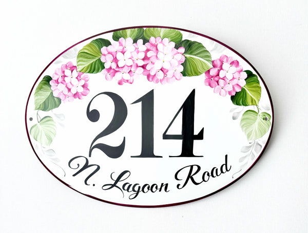 Oval-shaped house number plaque hand-painted with pink hydrangea and green leaves on a white background