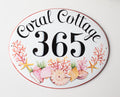 ceramic house number plaque hand painted with pink corals and shells. the house number is painted in center i black color and the name is on the top.