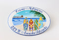 ceramic house sign oval shaped, hand painted with a central beach scene with colored surfboards on a beach, an ocean view, a pier, and a palm branch. the name is painted curved on top and the address on the bottom