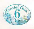 Ceramic Address plaque oval shaped hand painted with blue and teal corals and shells; the number is painted in blue in the center and the address on the top
