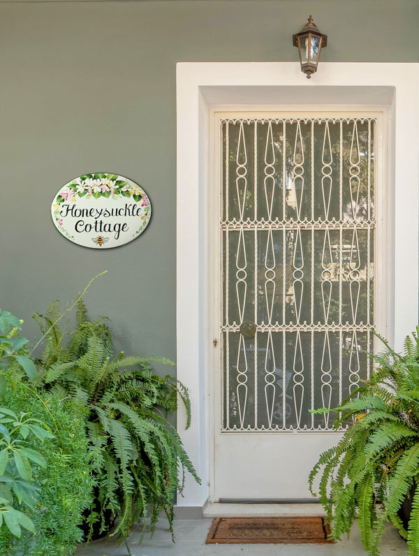 ceramic house sign hand-painted with honeysuckle and bee, mounted on a wall of a front door cottage