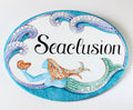 oval ceramic beach house sign hand painted with mermaid and blue waves  in mosaic style, the name is painted in black cursive
